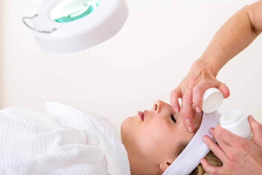 Beautician applying cream on the face of a woman.